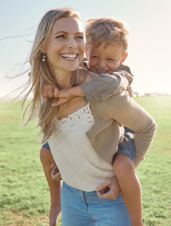 Image of a smiling woman holding her smiling child on back